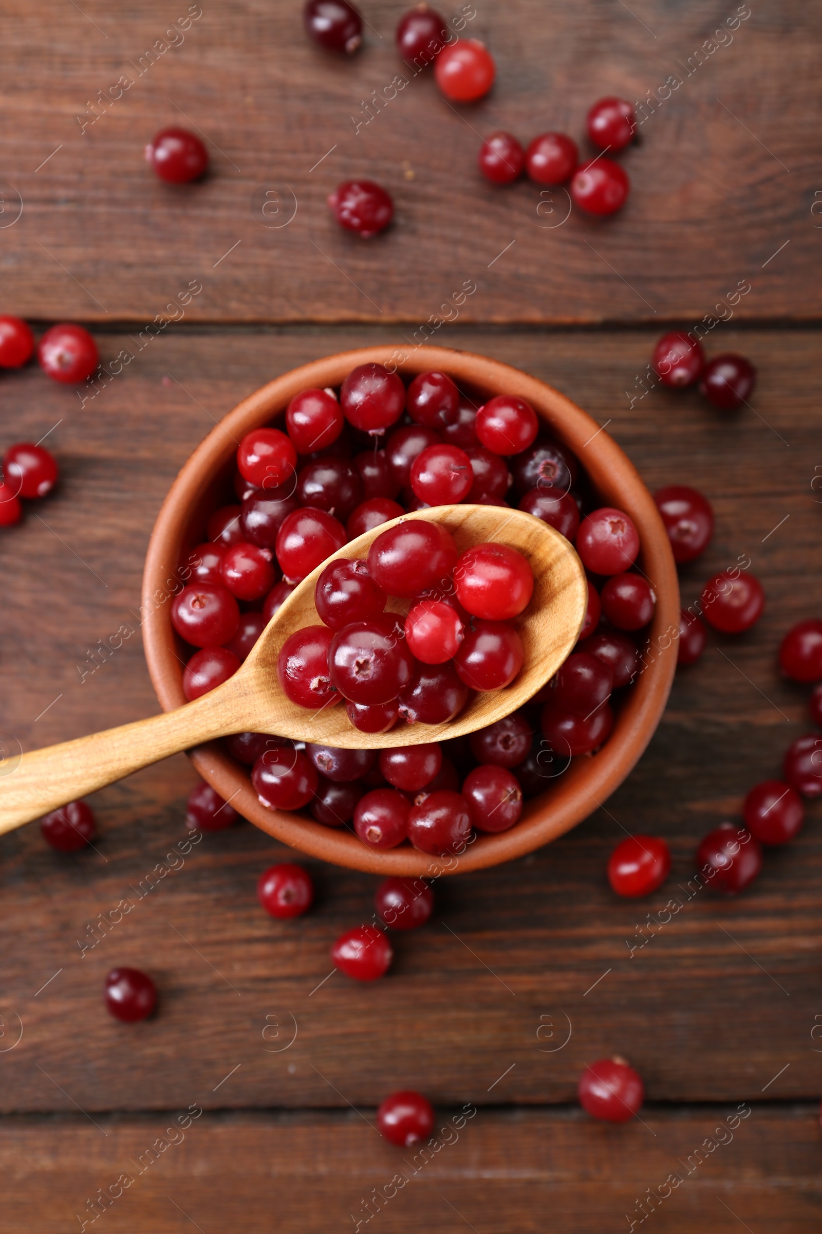 Photo of Fresh ripe cranberries in bowl and spoon on wooden table, flat lay