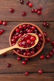 Photo of Fresh ripe cranberries in bowl and spoon on wooden table, flat lay