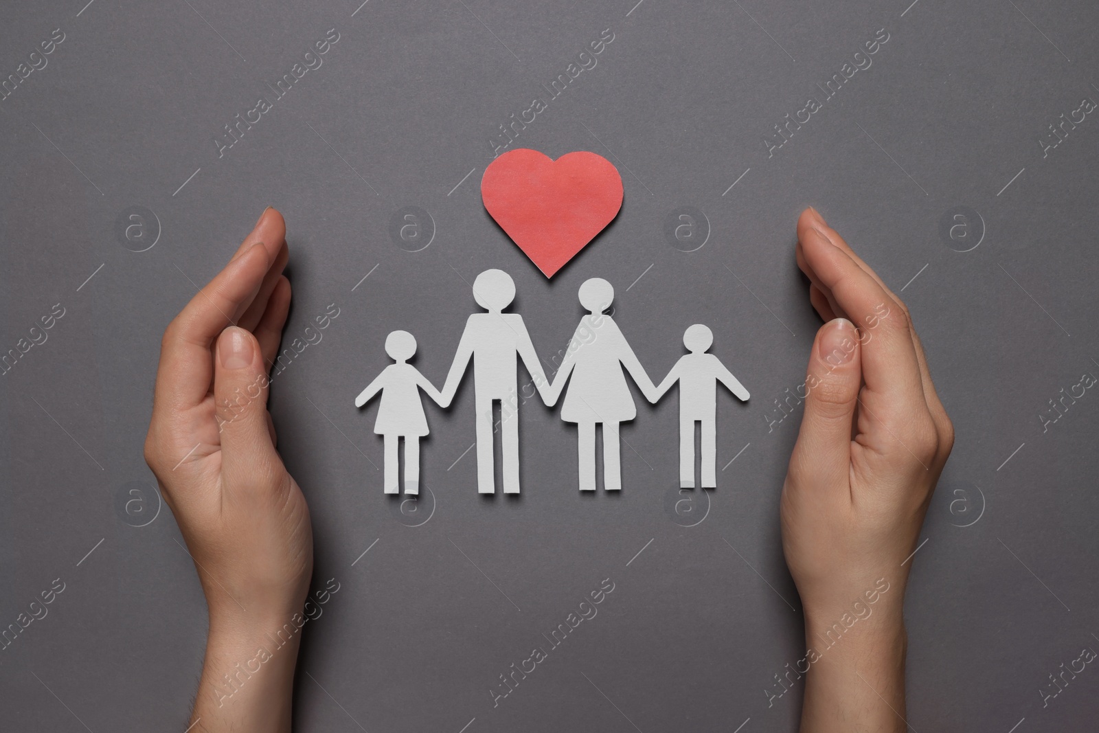 Photo of Woman protecting paper family figures and red heart on grey background, top view. Insurance concept