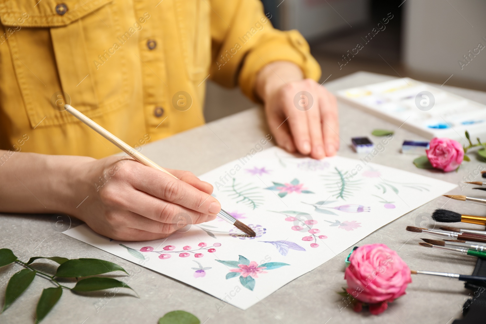 Photo of Woman painting flowers with watercolor at grey stone table, closeup