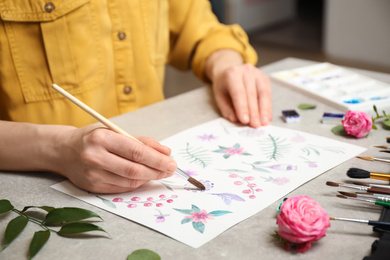 Woman painting flowers with watercolor at grey stone table, closeup