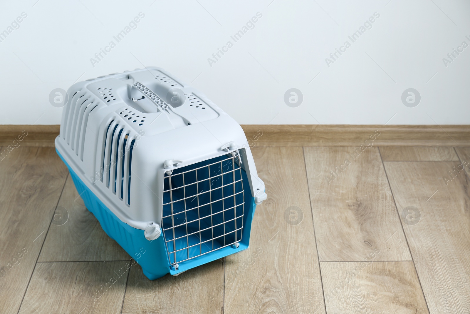 Photo of Light blue pet carrier on floor near white wall. Space for text