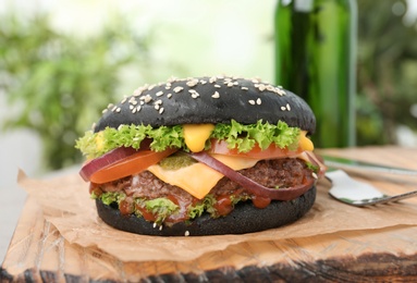 Board with black burger on blurred background, closeup