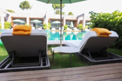 Photo of Sunbeds near swimming pool at luxury resort, blurred view