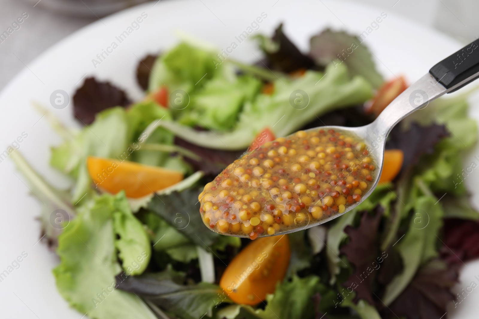 Photo of Spoon with tasty vinegar based sauce (Vinaigrette) over salad on table, closeup