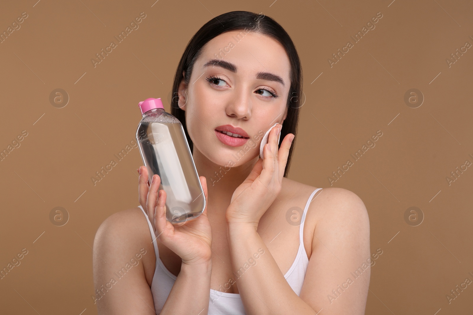 Photo of Beautiful woman removing makeup with cotton pad on beige background