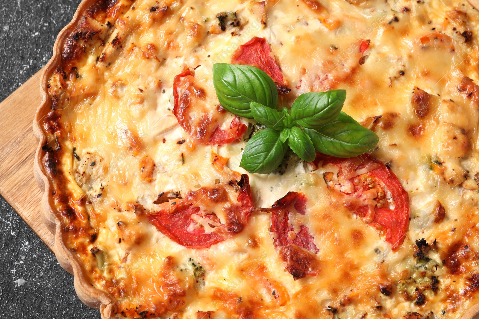 Photo of Tasty quiche with tomatoes, basil and cheese on dark textured table, top view