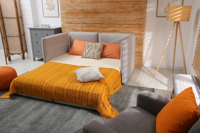 Photo of Room interior with sofa unfolded into bed near wooden wall