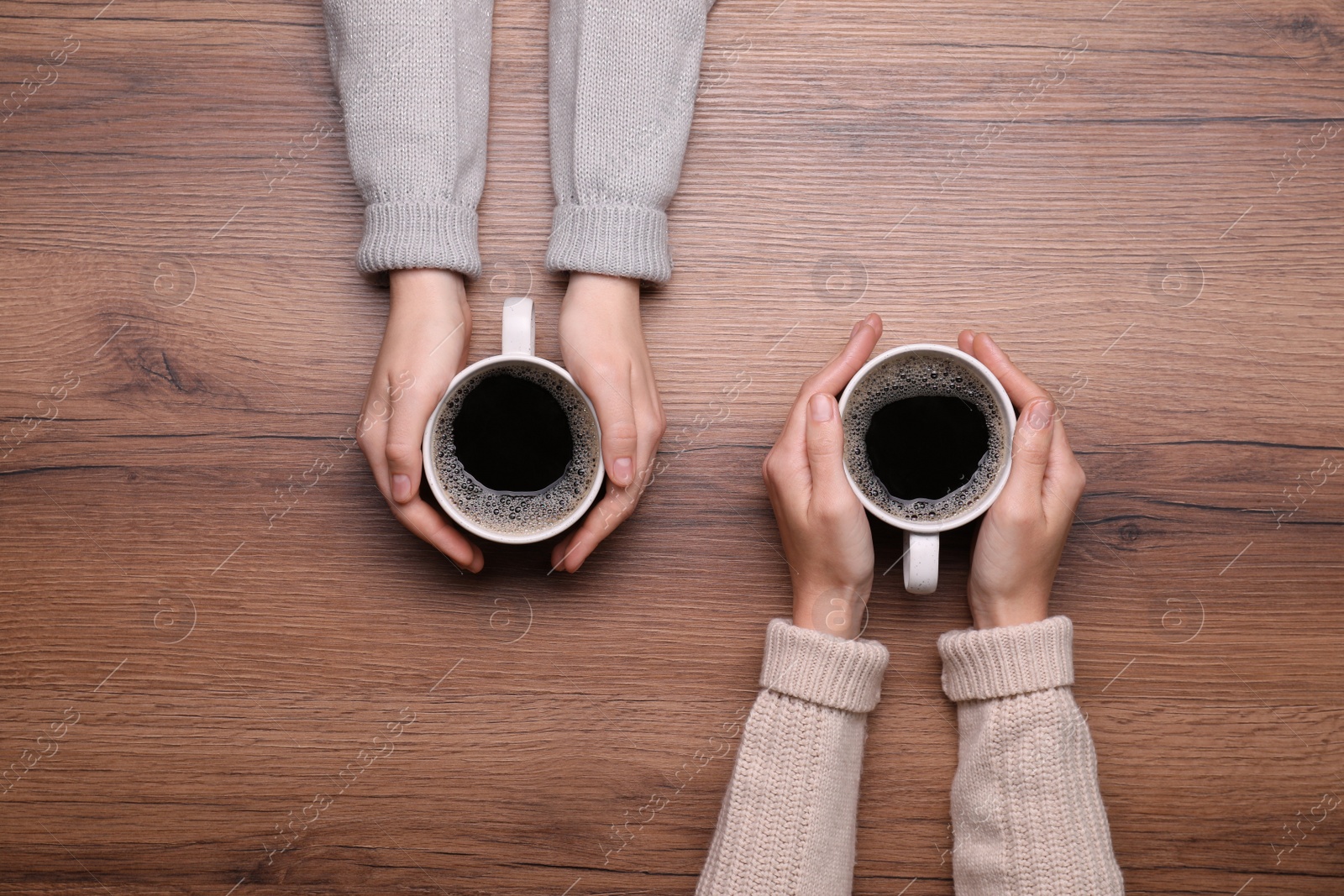 Photo of Women with cups of coffee at wooden table, top view