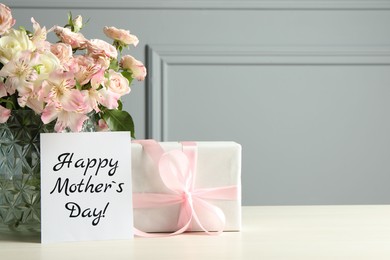 Image of Happy Mother's Day greeting card, gift box and bouquet of beautiful flowers on white wooden table