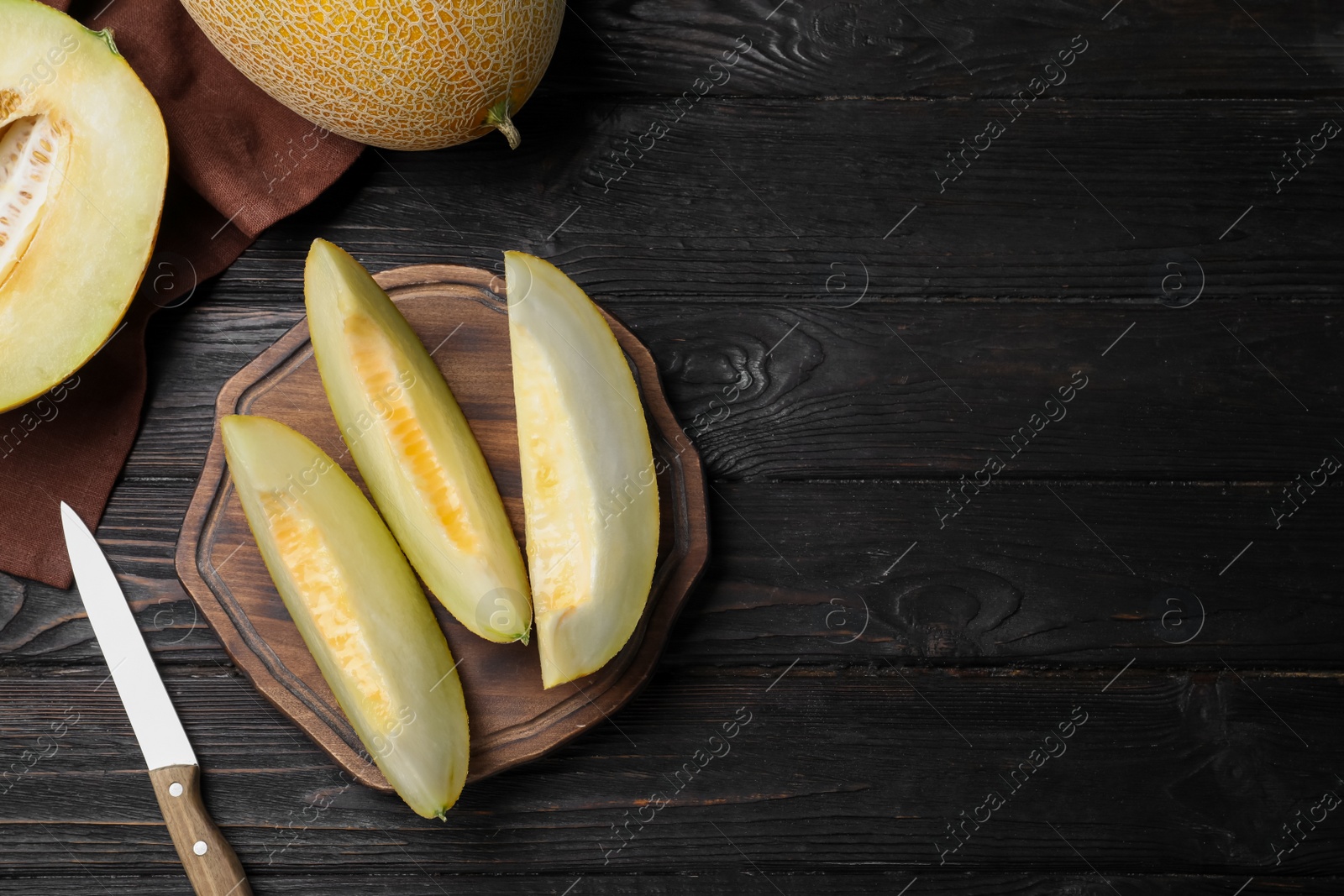 Photo of Pieces of delicious honeydew melon on black wooden table, flat lay. Space for text