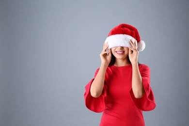 Photo of Young beautiful woman in Santa hat on grey background. Christmas celebration