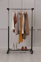 Rack with different stylish clothes near grey wall indoors