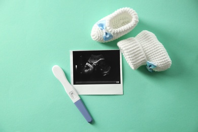 Ultrasound picture, baby shoes and pregnancy test on color background, top view