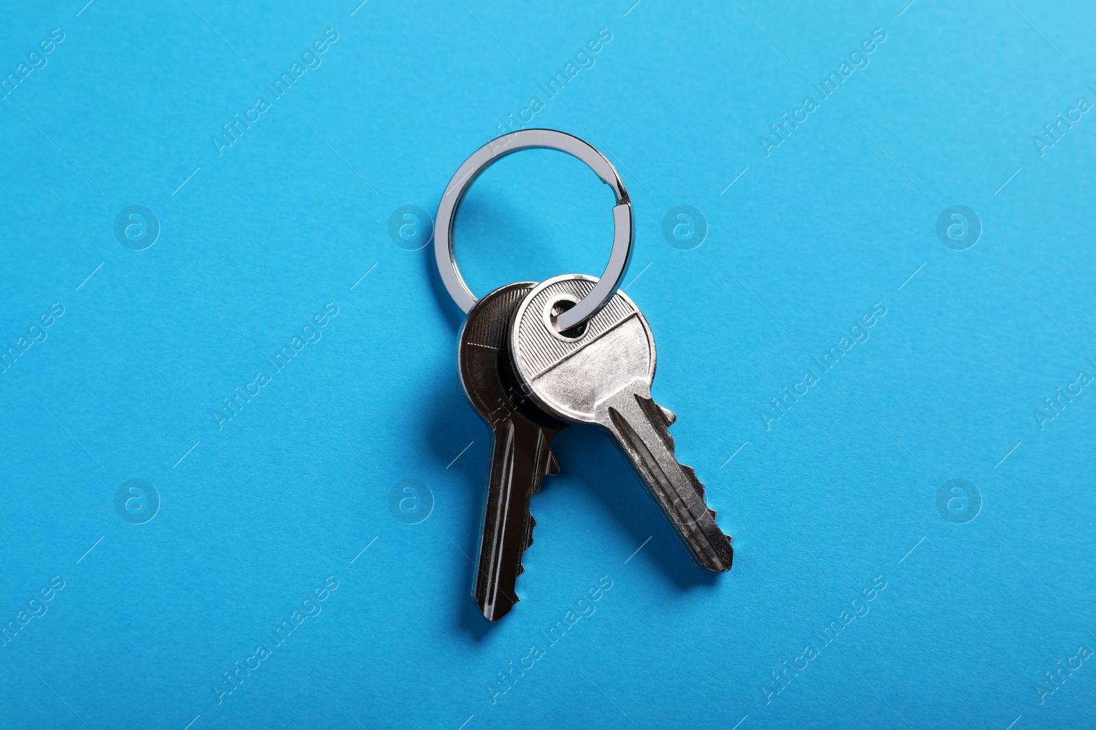 Photo of House keys on light blue background, top view. Real estate agent services