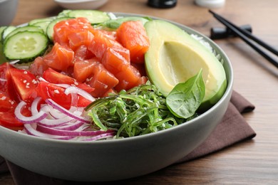 Photo of Delicious poke bowl with salmon and vegetables served on wooden table, closeup