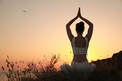 Photo of Woman meditating outdoors at sunset, back view. Space for text