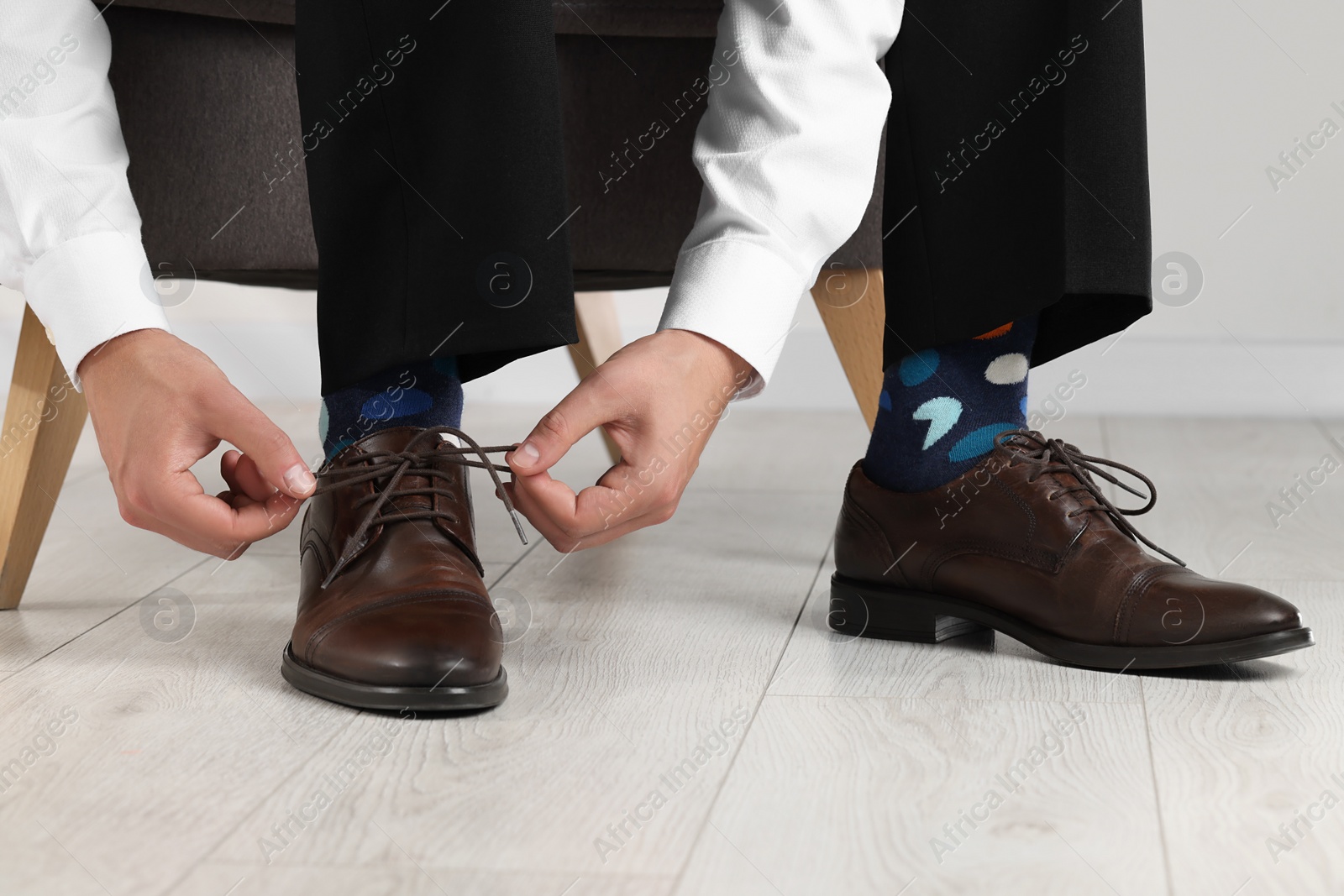 Photo of Man with colorful socks putting on stylish shoes indoors, closeup