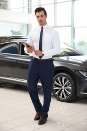 Photo of Young salesman with tablet near car in modern dealership