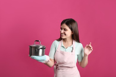 Happy young woman with cooking pot on pink background