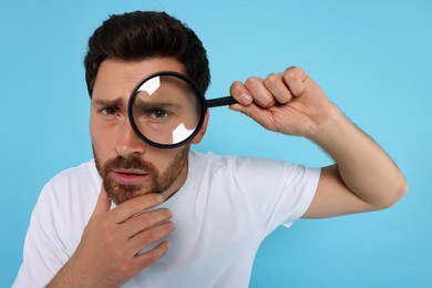Photo of Man looking through magnifier glass on light blue background
