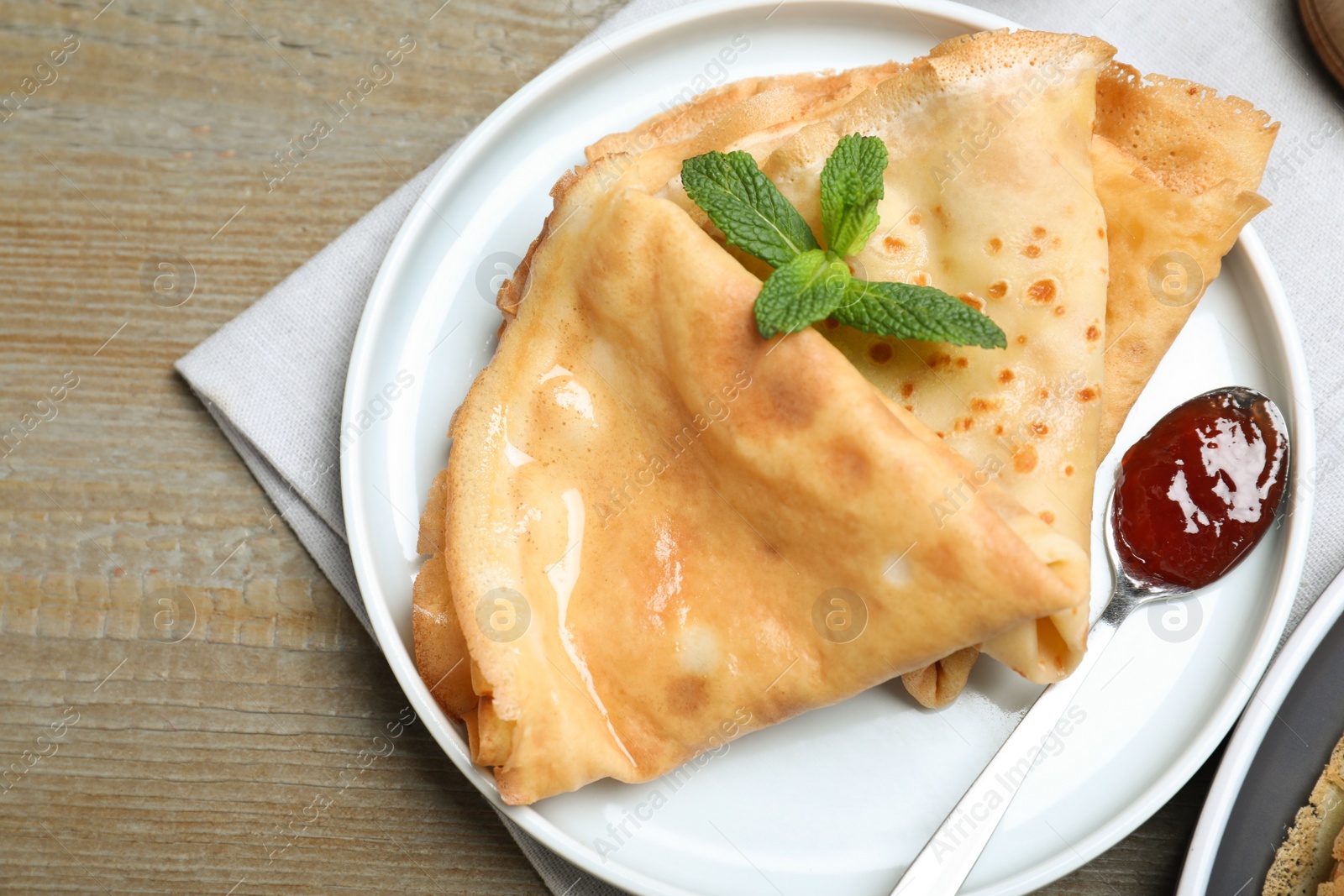 Photo of Delicious crepes served with mint and jam on grey wooden table, top view