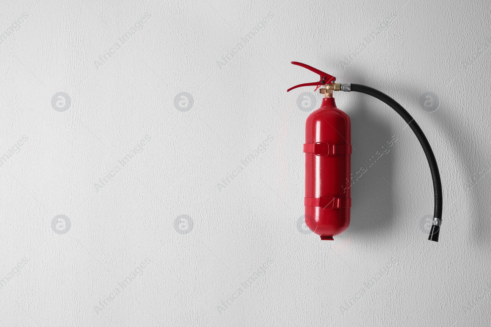 Photo of Fire extinguisher hanging on white wall. Space for text