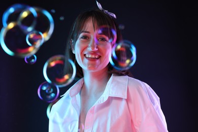 Photo of Portrait of happy woman among bubbles on dark background