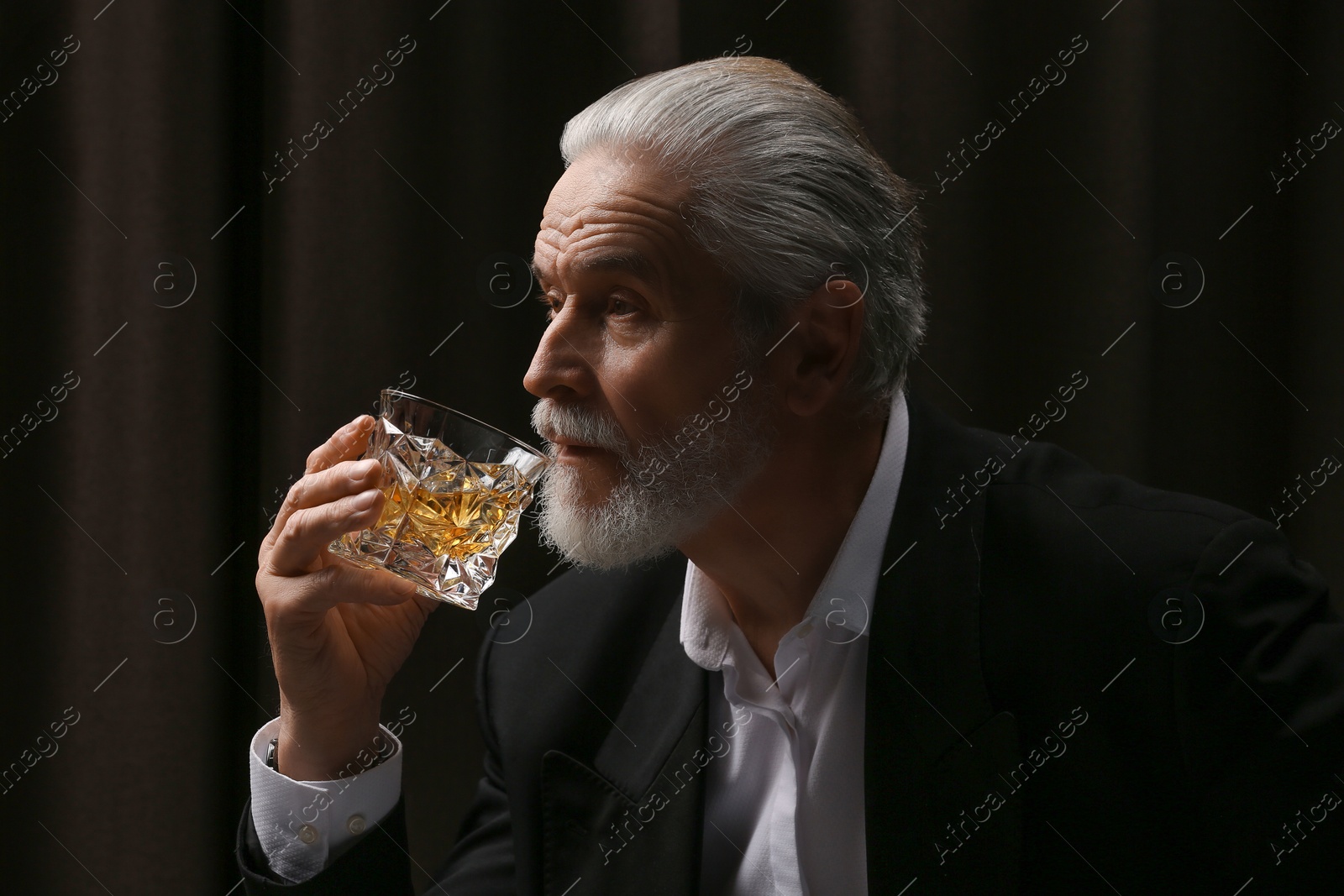 Photo of Senior man in suit drinking whiskey on black background