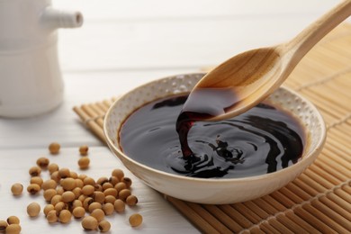 Taking tasty soy sauce from bowl with spoon on white wooden table, closeup