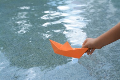Kid launching small orange paper boat on water outdoors, closeup. Space for text