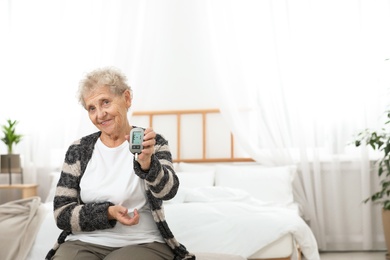 Senior woman holding digital glucose meter at home. Diabetes control