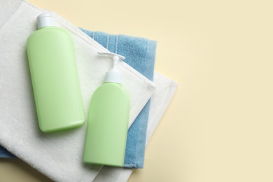Bottles of shampoo and towels on color background, top view with space for text