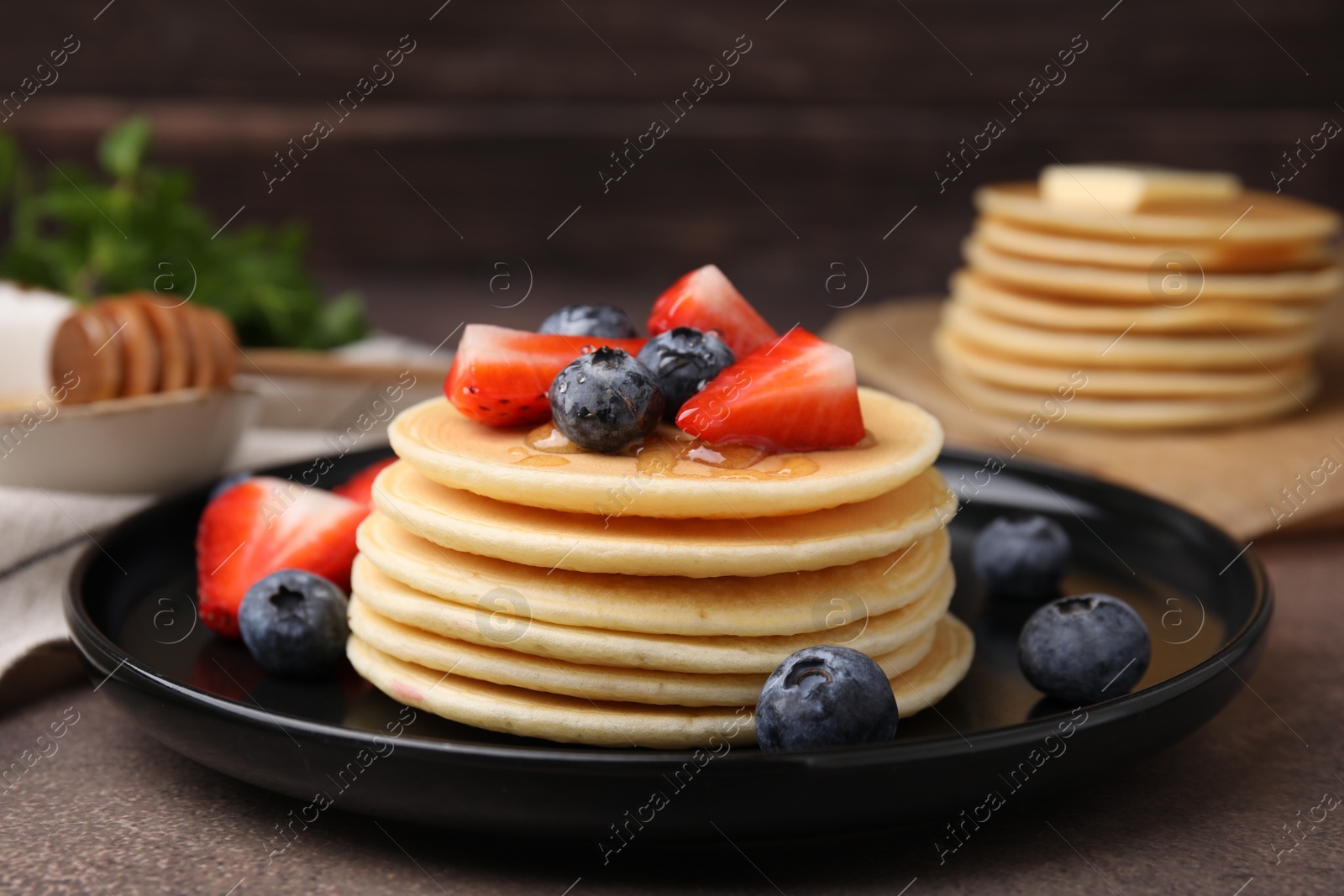 Photo of Delicious pancakes with strawberries and blueberries on brown textured table, closeup