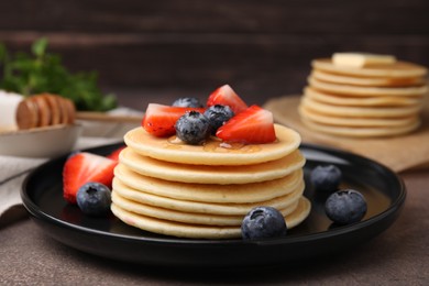 Photo of Delicious pancakes with strawberries and blueberries on brown textured table, closeup