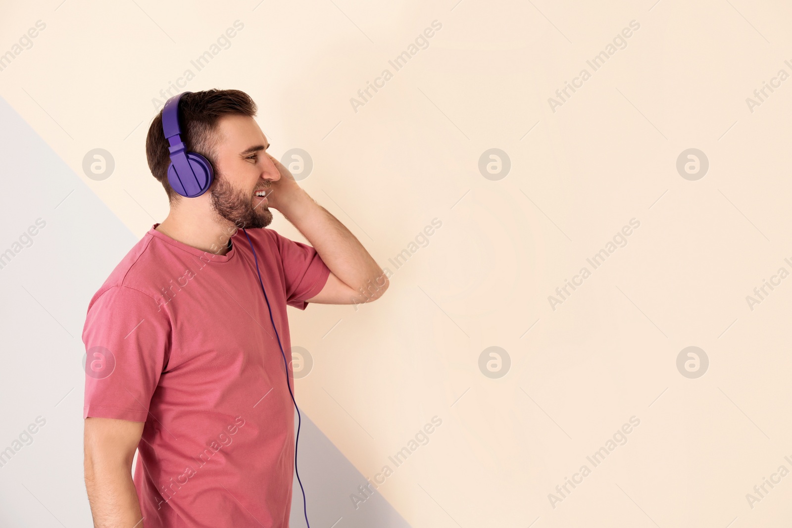 Photo of Handsome man enjoying music in headphones on color background. Space for text