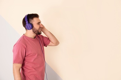 Photo of Handsome man enjoying music in headphones on color background. Space for text