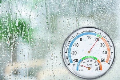 Image of Mechanical hygrometer with thermometer on glass with water drops. Space for text