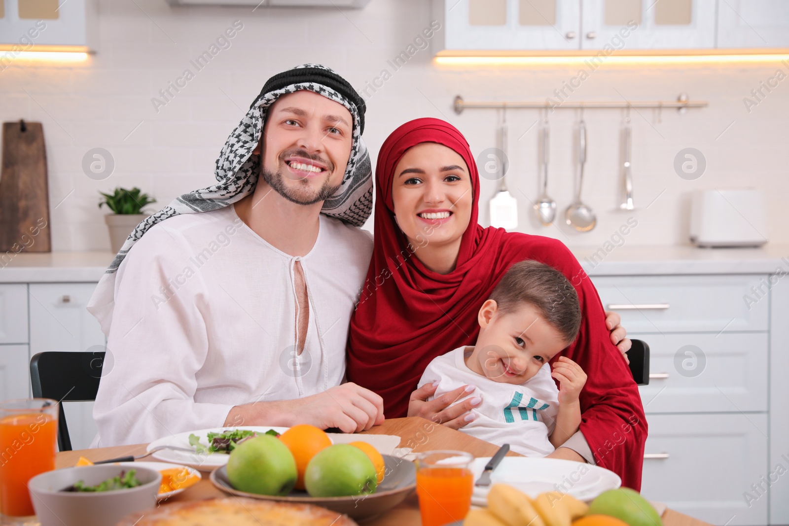 Photo of Happy Muslim family eating together at table in kitchen