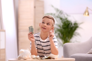 Photo of Little boy with broken piggy bank and money at home