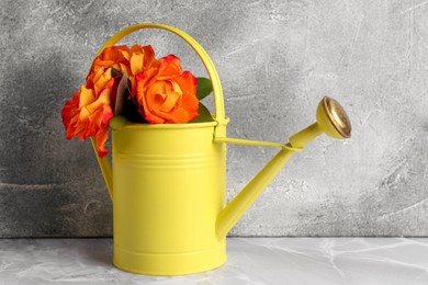 Beautiful bouquet of orange roses in watering can on light grey table