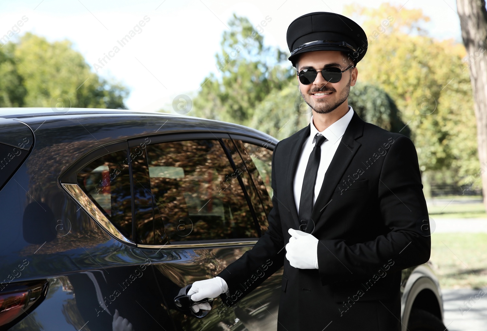 Photo of Young handsome driver opening luxury car door. Chauffeur service