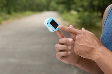 Young man checking pulse with medical device after training in park, closeup. Space for text