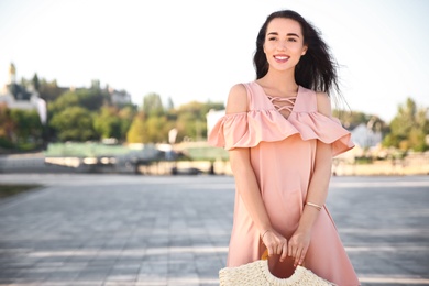 Beautiful young woman in stylish pink dress with handbag on city street