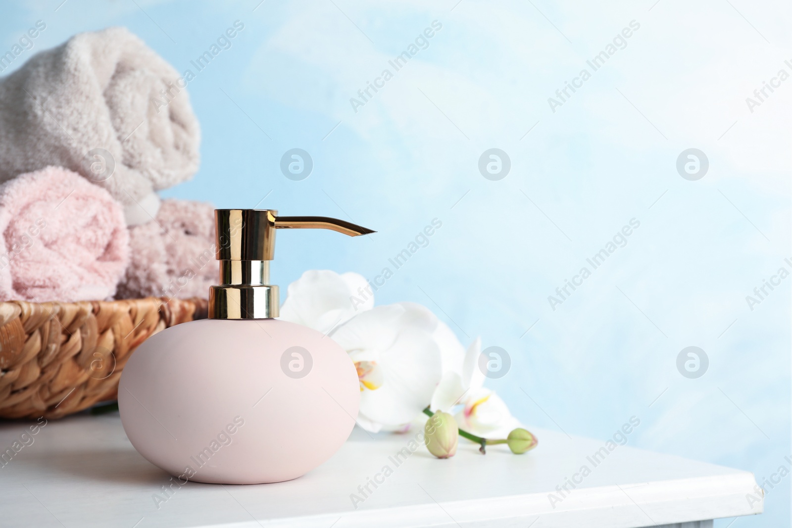 Photo of Stylish soap dispenser, towels in wicker basket and flowers on table. Space for text