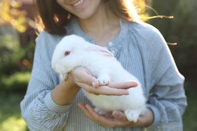 Photo of Happy woman holding cute rabbit outdoors on sunny day, closeup