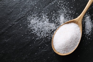 Organic white salt in spoon on black table, top view. Space for text