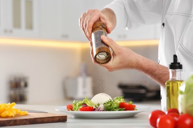 Photo of Professional chef adding pepper into delicious salad at marble table in kitchen, closeup. Space for text