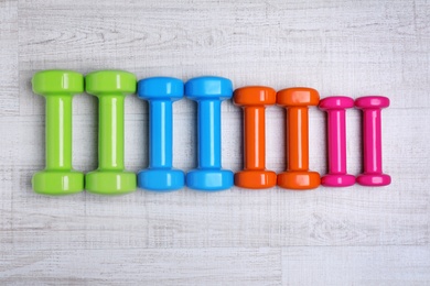 Many colorful dumbbells on table, flat lay. Fitness equipment