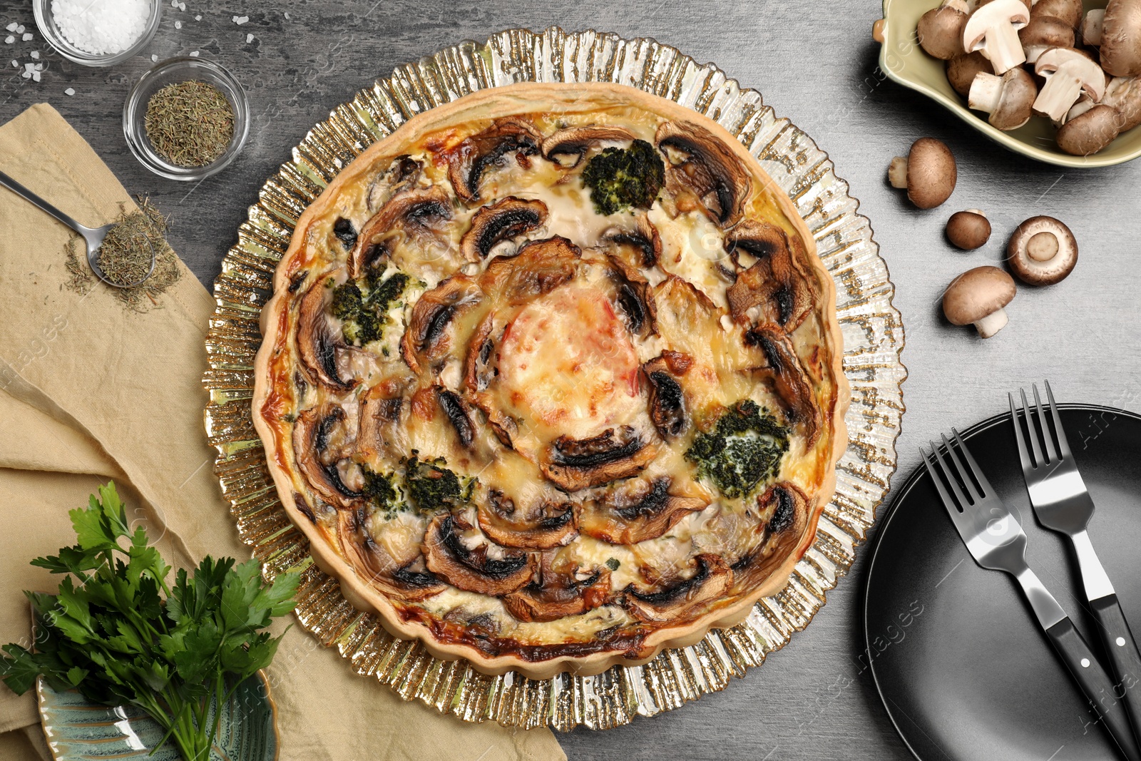 Photo of Delicious quiche with mushrooms and ingredients on dark grey table, flat lay